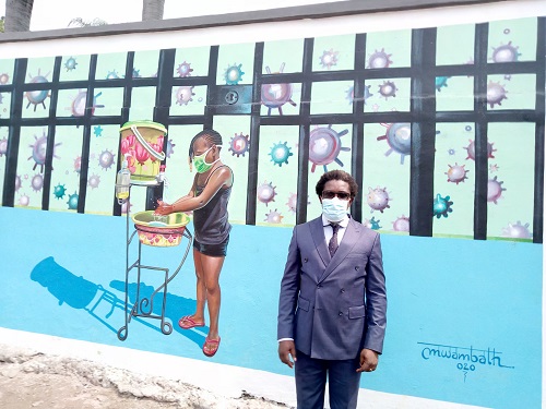 Henri Kalama devant la fresque du peintre Théo Mwamba évoquant le Lavage des mains