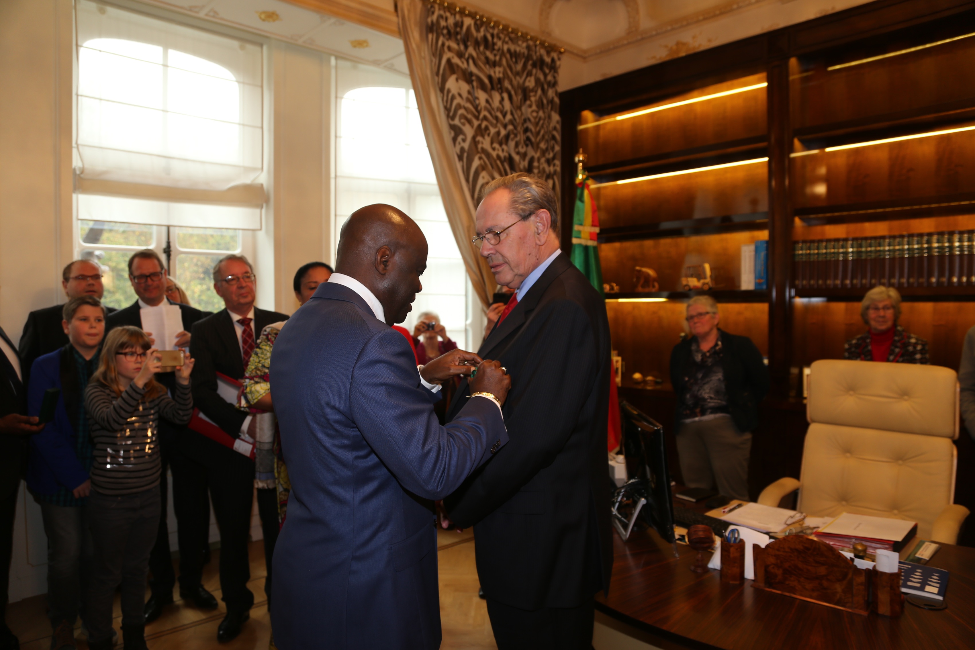 Meüs van der Poel, très ému, reçoit des mains de l'ambassadeur Roger Julien Menga, au nom du président de la République, les insignes de chevalier dans l'ordre du dévouement congolais 