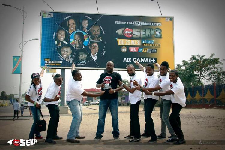 Les jeunes humoristes de la team Toseka et Ados Ndombasi face à un panneau du festival sur l’avenue de La libération (ex-24 novembre)